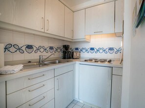 A kitchen with white cabinets, a stainless steel sink, and a coffee maker. - Apartment 14 (St. Peter-Ording)
