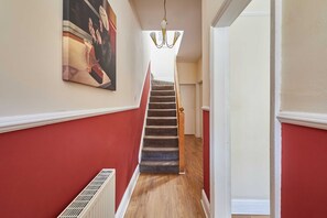 A hallway with a staircase, a radiator, and a chandelier. - Host & Stay | Norwood Street (Scarborough)