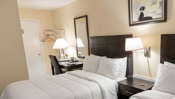 A hotel room with two beds, a desk, a chair, a lamp, and a framed picture on the wall. - North Star Motel (Shelburne)