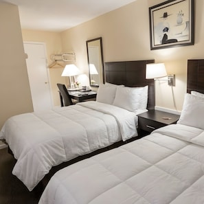 Een hotelkamer met twee bedden, een bureau, een stoel, een lamp en een lijst aan de muur.