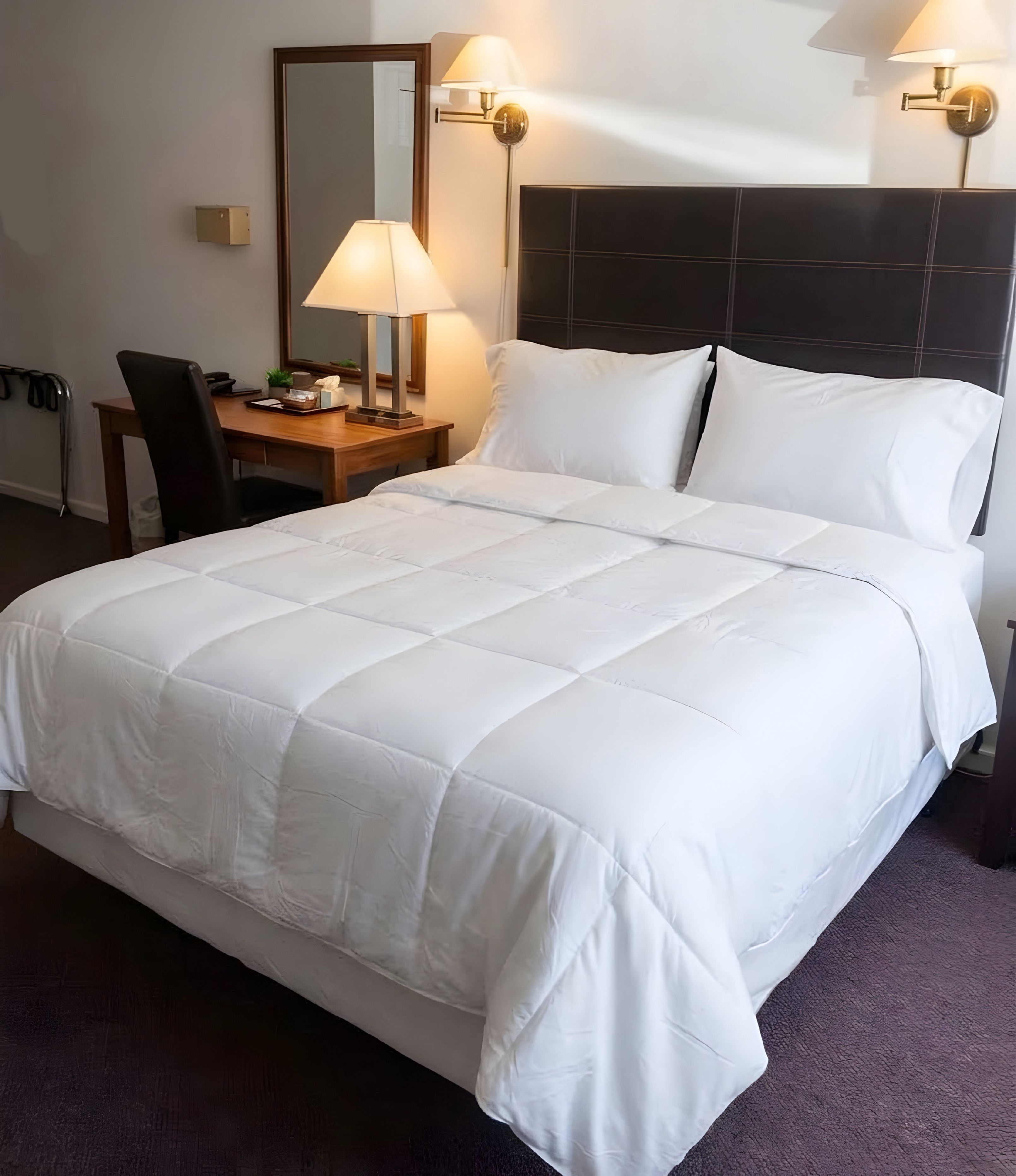 Een hotelkamer met een groot bed, een nachtkastje met een lamp en een stoel.