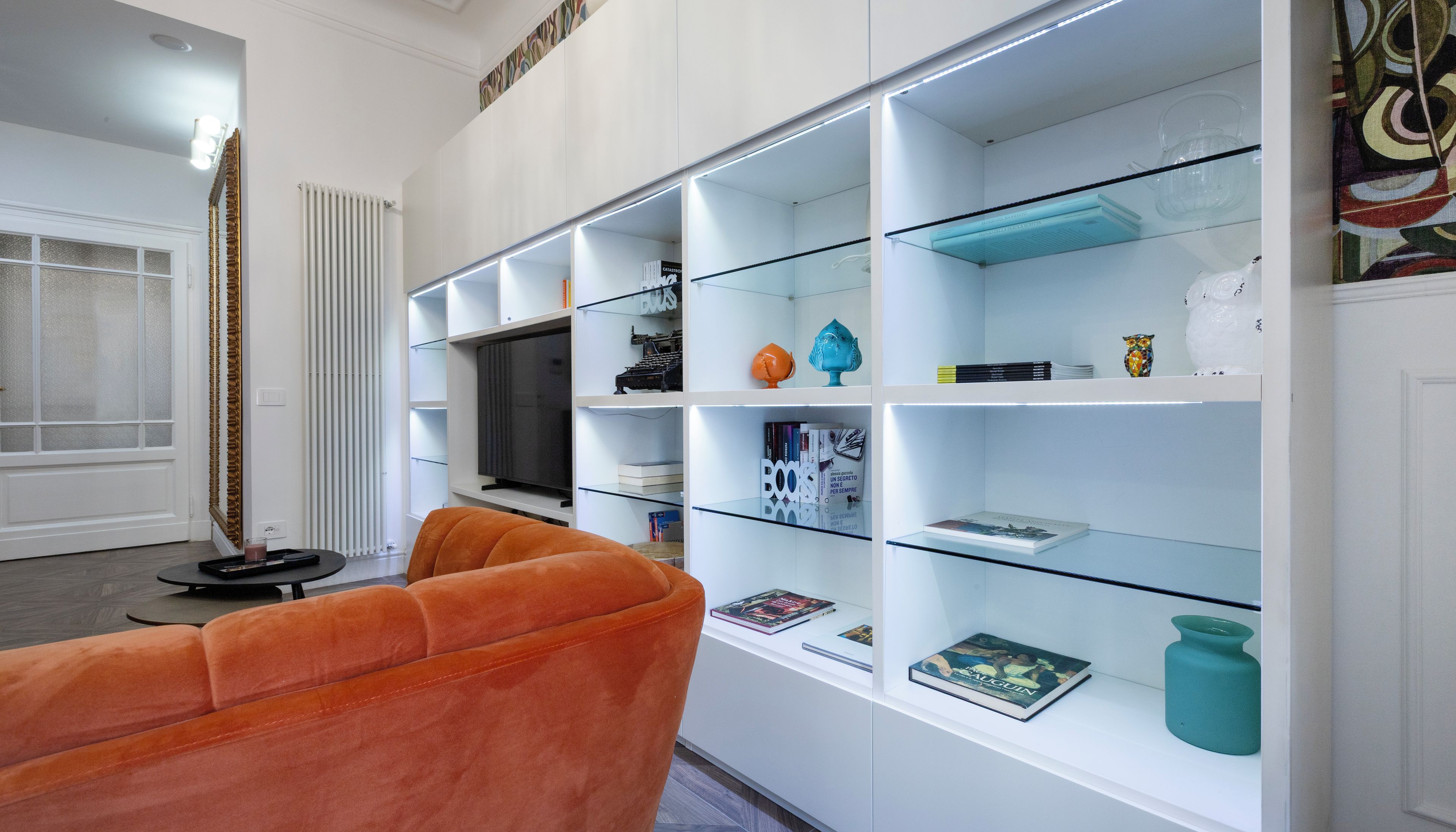 En moderne stue med sofa, fjernsyn og et reolsystem med glasfronter, fyldt med bøger og pynteting.