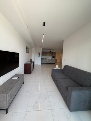 A modern living room with a flat-screen TV, a grey sofa, and a coffee table. - Modern Apartment in Paceville Steps from Beach (San Ġiljan)