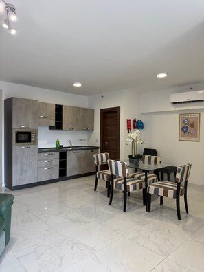 A modern kitchen with grey cabinets, a built-in oven, and a dining area with striped chairs and a glass table. - Modern Apartment in Paceville Steps from Beach (San Ġiljan)