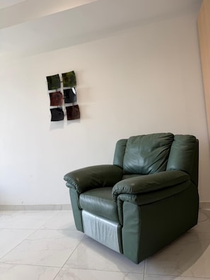 A green leather armchair in a room with a white wall and a tiled floor. - Modern Apartment in Paceville Steps from Beach (San Ġiljan)