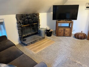A living room with a stone fireplace, a flat-screen TV mounted on the wall, a wooden cabinet, and a round leather ottoman. - guhos ranch (Big Bear Lake)