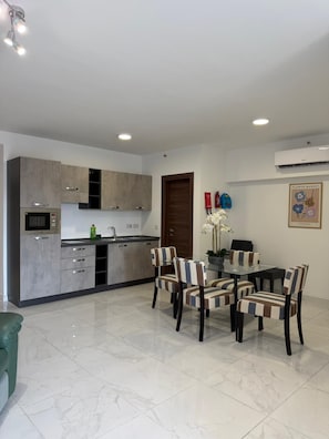 A modern kitchen with grey cabinets, a built-in oven, and a dining area with striped chairs and a glass table. - Modern Apartment in Paceville Steps from Beach (San Ġiljan)