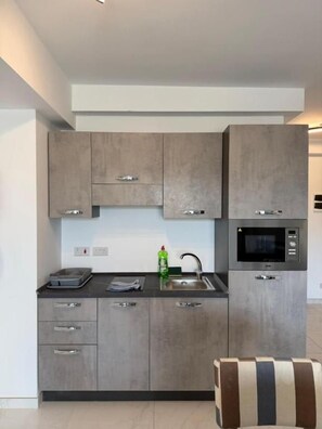 A modern kitchen with grey cabinetry, a microwave, and a sink. - Modern Apartment in Paceville Steps from Beach (San Ġiljan)