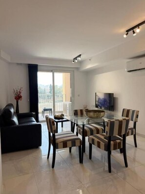 A modern living room with a glass dining table, striped chairs, a sofa, and a flat-screen TV. - Modern Apartment in Paceville Steps from Beach (San Ġiljan)