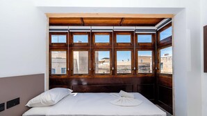 Une chambre à coucher avec un lit, une tête de lit en bois et une vue sur les immeubles à travers de grandes fenêtres.