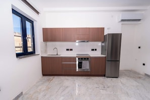 Una cucina compatta con forno integrato, frigorifero in acciaio inox e pensili in legno.