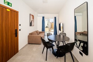 Ein Hotelzimmer mit Holztür, einem beigefarbenen Sofa, einem runden Tisch mit Stühlen und einem großen Spiegel an der Wand.