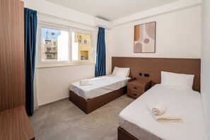 Quarto de hotel com duas camas, janela com cortinas, cabeceira de madeira e uma obra de arte pendurada na parede.