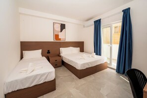 Hotellihuone, jossa on kaksi sänkyä, työpöytä, tuoli ja näkymä ulos.