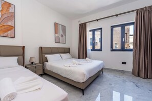 Una camera d'albergo con due letti, un comodino, una lampada e vista sull'esterno da una finestra.