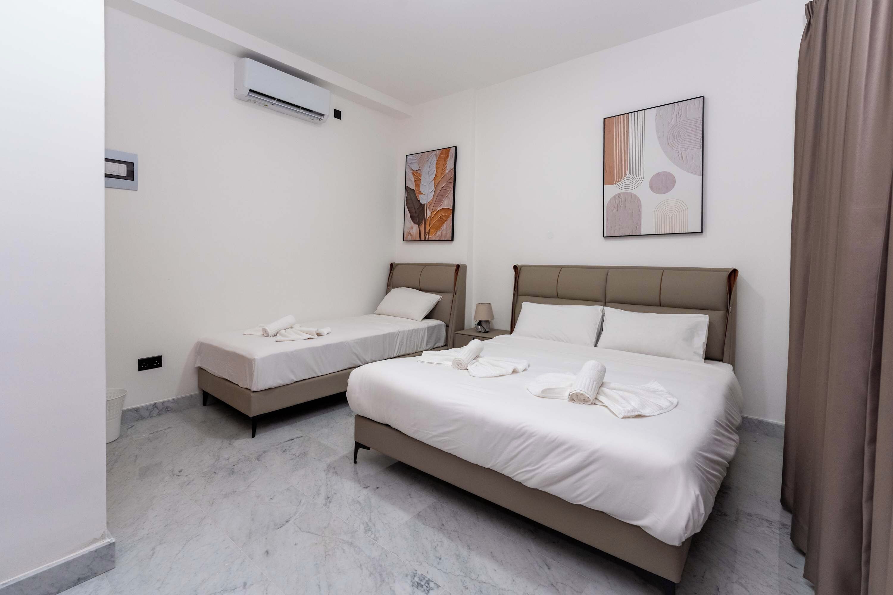 Una camera d'albergo con due letti, un condizionatore d'aria a parete e due quadri astratti.