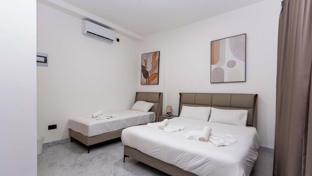 Une chambre d’hôtel avec deux lits, un climatiseur fixé au mur et deux tableaux abstraits.