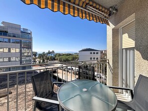 Ein Balkon mit Glastisch und Stühlen, mit Blick auf eine Straße mit Gebäuden und blauem Himmel.