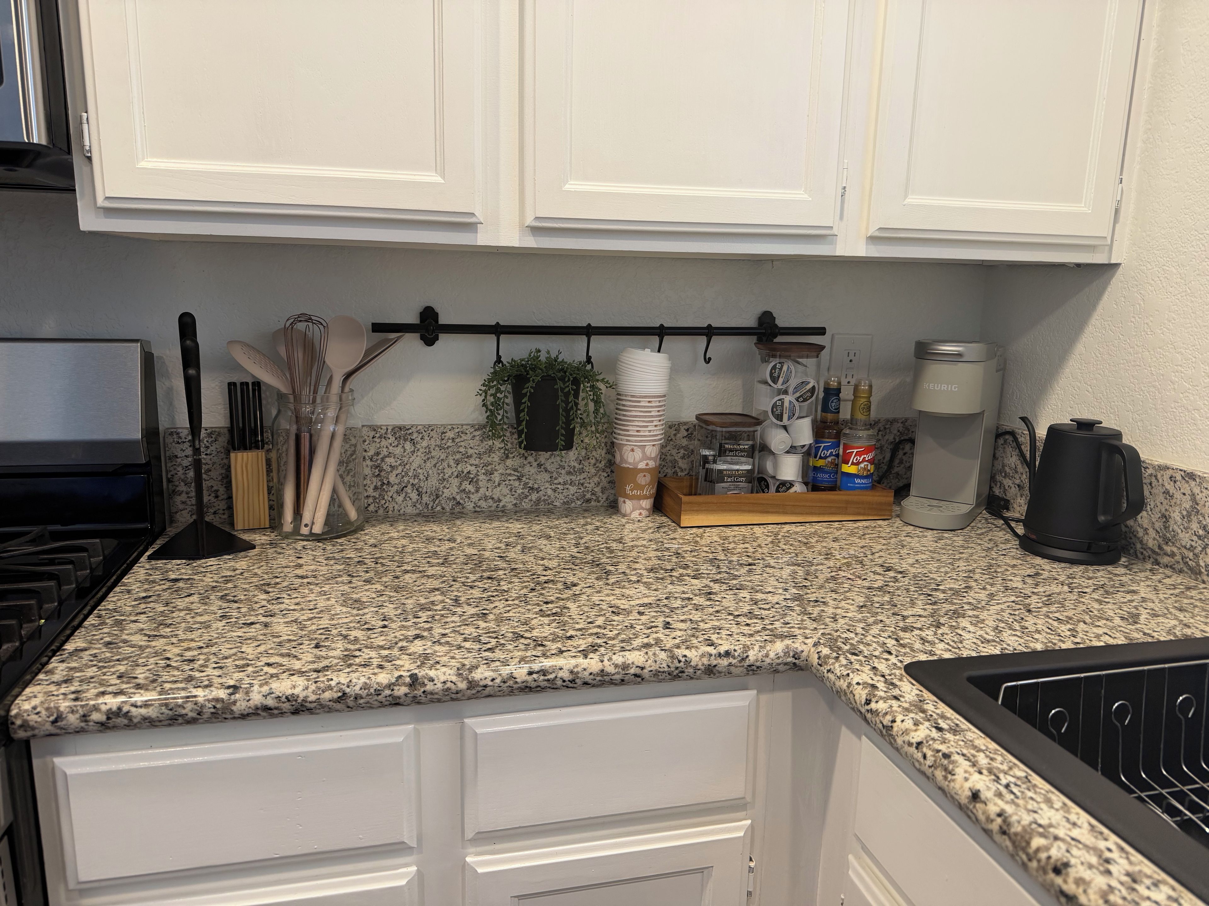 A kitchen with granite countertops, white cabinets, a coffee maker, and various kitchen utensils.