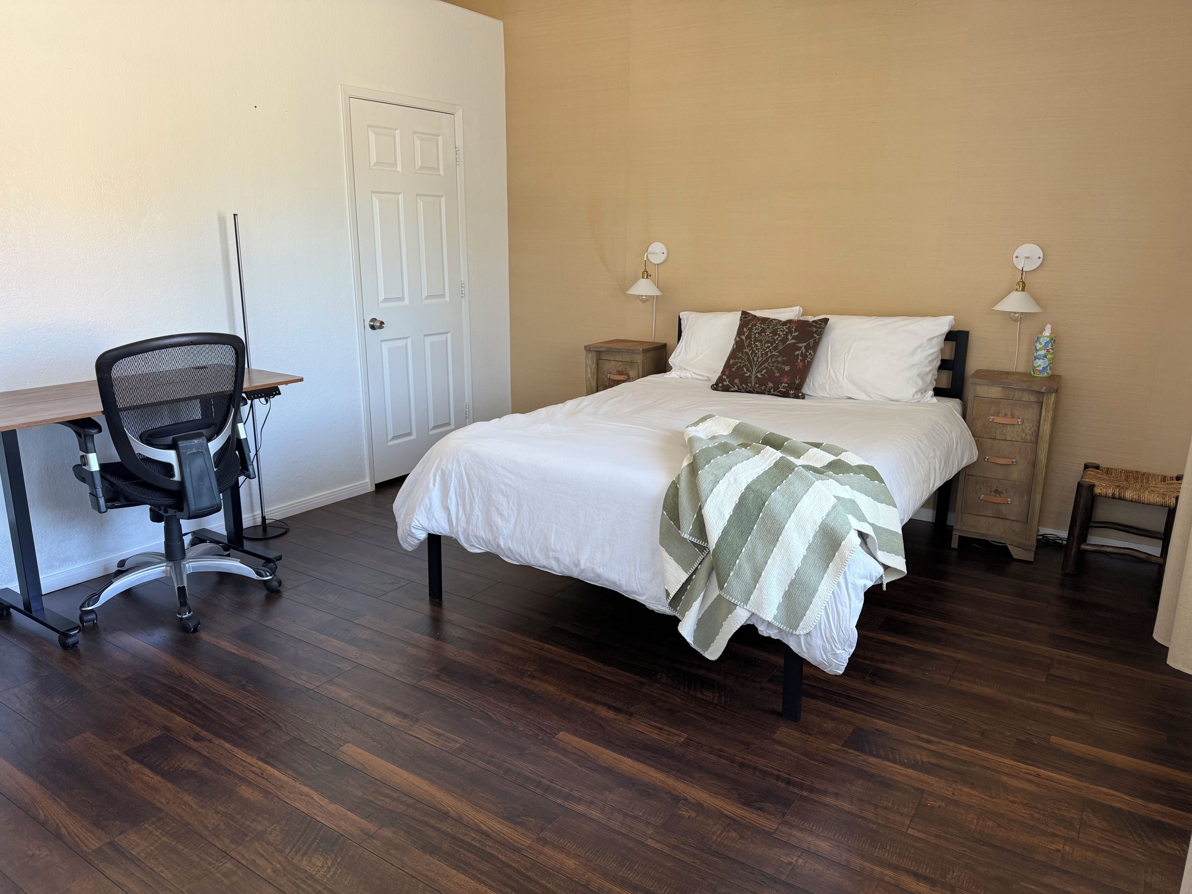 A bedroom with a bed, bedside tables, a desk, and a chair.