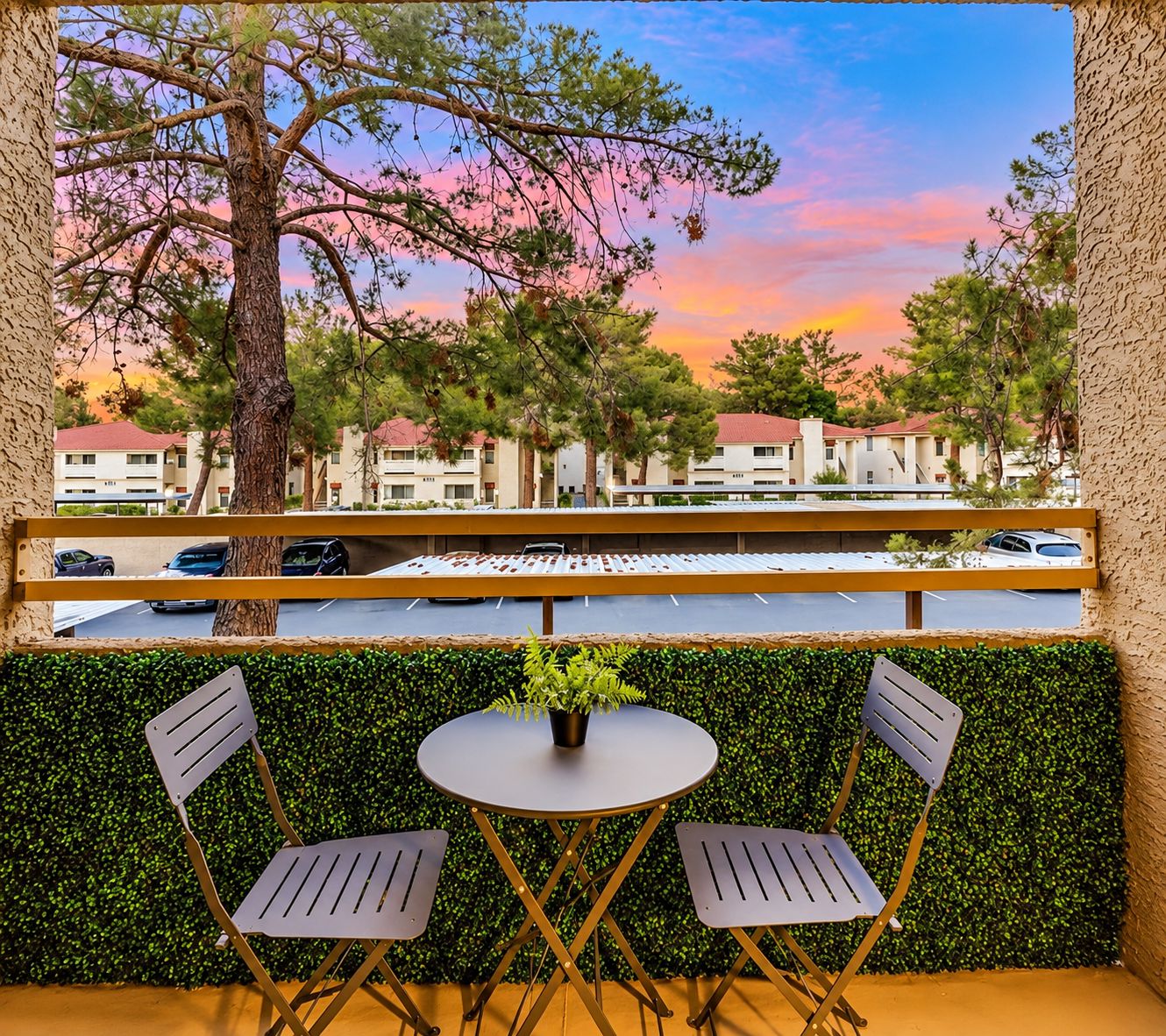 A balcony with two chairs and a table, overlooking a parking area and buildings.
