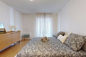 Ein Schlafzimmer mit einem Bett, einem Schreibtisch, einem Stuhl, einem Heizkörper und einem Fenster mit Vorhängen.
