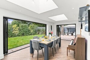 A modern dining area with a large table, chairs, and a view of a garden. - Ashcombe House • Sleeps 9 • Pool Table • Snug Room • SkyTV • Xbox • Driveway Parking • Yoko Property (Worthing)