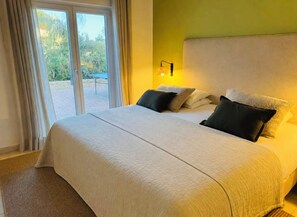 A hotel room with a large bed, a nightstand with a lamp, and a view of the outdoors through a sliding door. - Villa Maris - Your Place in the Sun (Carvoeiro)