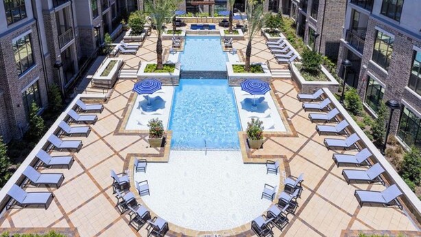 Área de piscina no terraço com espreguiçadeiras e uma piscina central, cercada por um edifício com vários andares e janelas.