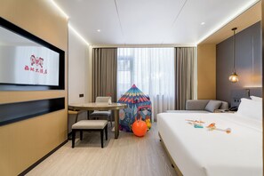 A hotel room with a bed, a desk, a chair, a colorful play tent, and a television on the wall.