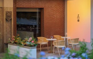 An outdoor seating area with wicker chairs and a table, a planter with flowers, and a hotel sign.
