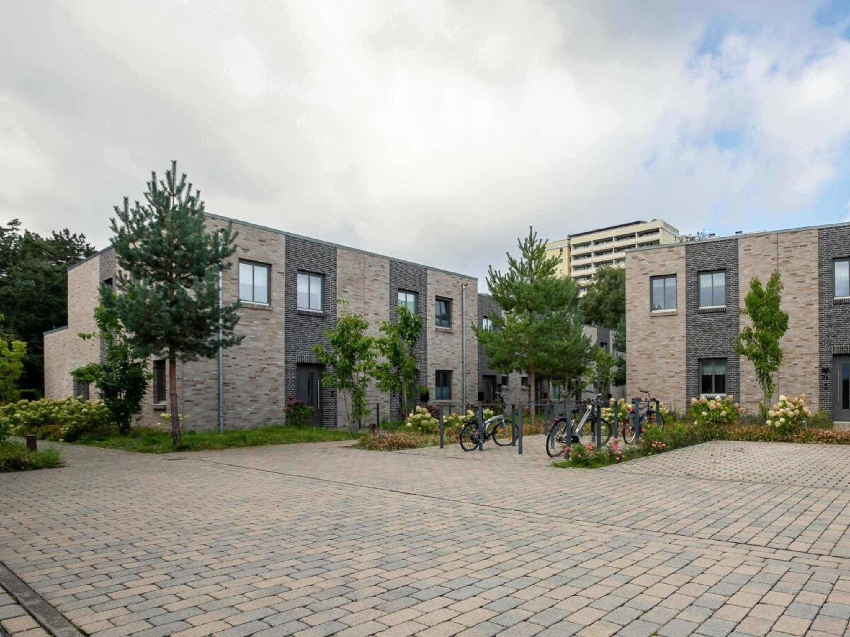 Un bâtiment moderne avec une façade en briques, de nombreuses fenêtres et une cour pavée où sont garés des vélos.