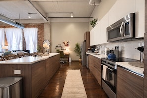 A modern kitchen with a central island, stainless steel appliances, and a brick wall. - The Bentley Collection - The Fitzgerald (Dallas)