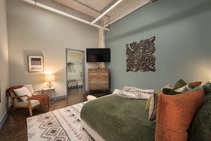 A bedroom with a bed, a dresser, a chair, a TV, and a wall-mounted decorative piece.