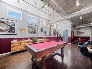 A pool table in a room with wooden flooring, pendant lighting, and wall-mounted artwork.