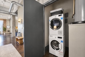 A laundry room with stacked washers and dryers, a wooden bench, and a clock on the wall.