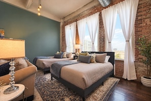 A hotel room with two beds, a sitting area with a lamp, and a view of the city. - The Bentley Collection - The Fitzgerald (Dallas)