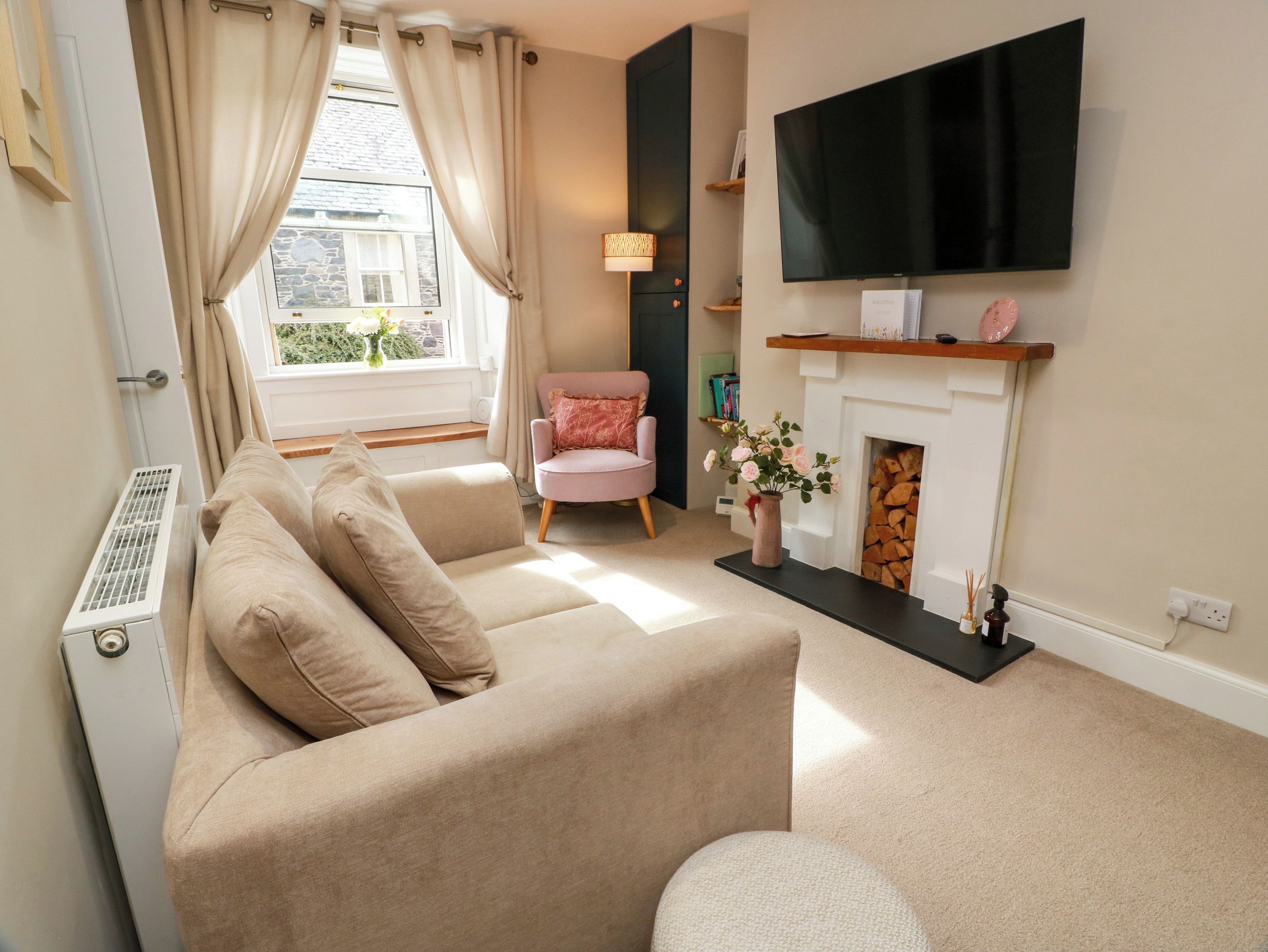 A living room with a beige sofa, a pink armchair, a fireplace, and a flat-screen TV mounted on the wall.