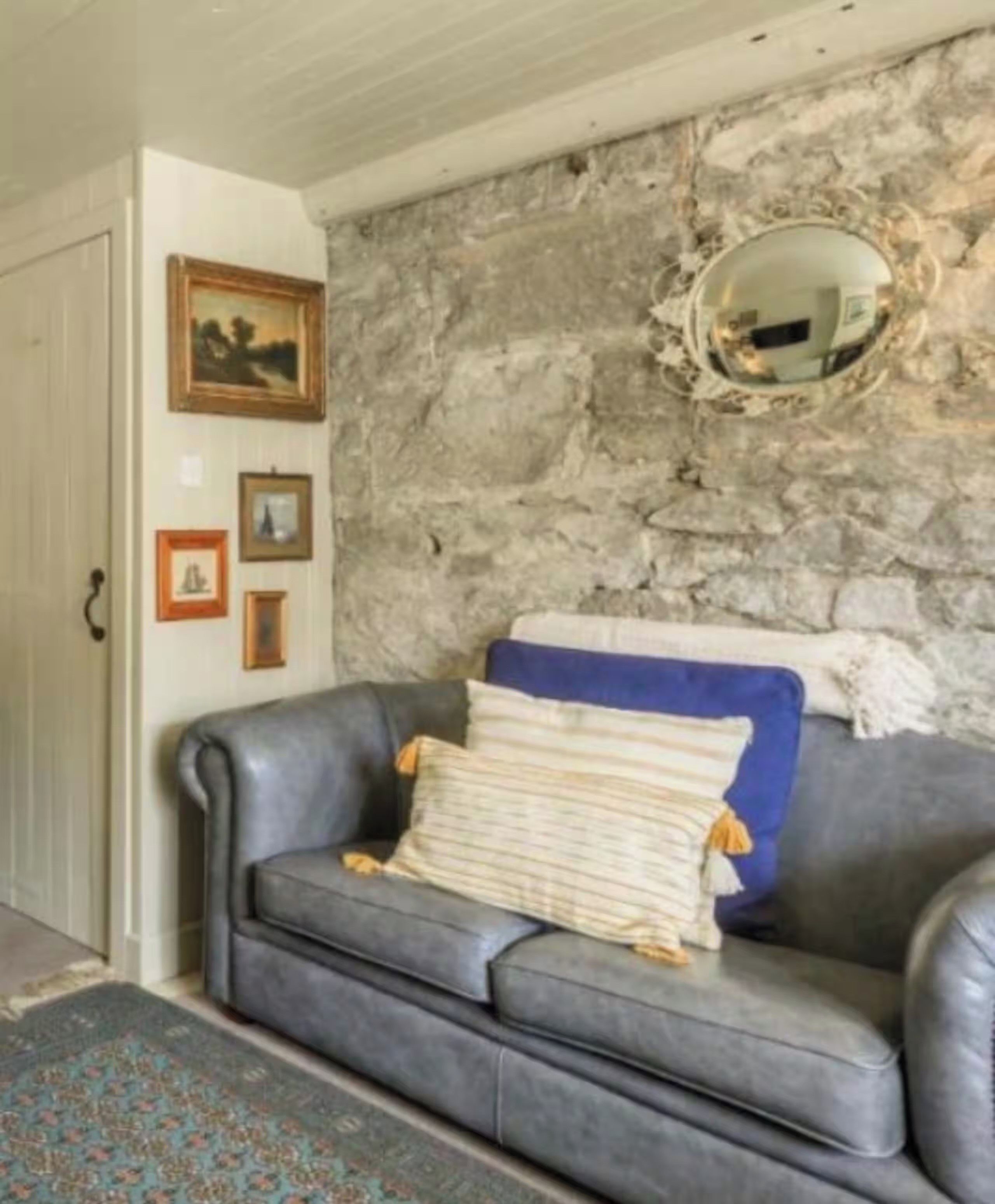 A room with a stone wall, a gray leather sofa, and a mirror.