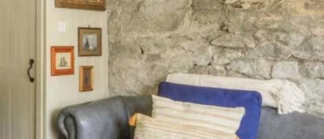 A room with a stone wall, a gray leather sofa, and a mirror.