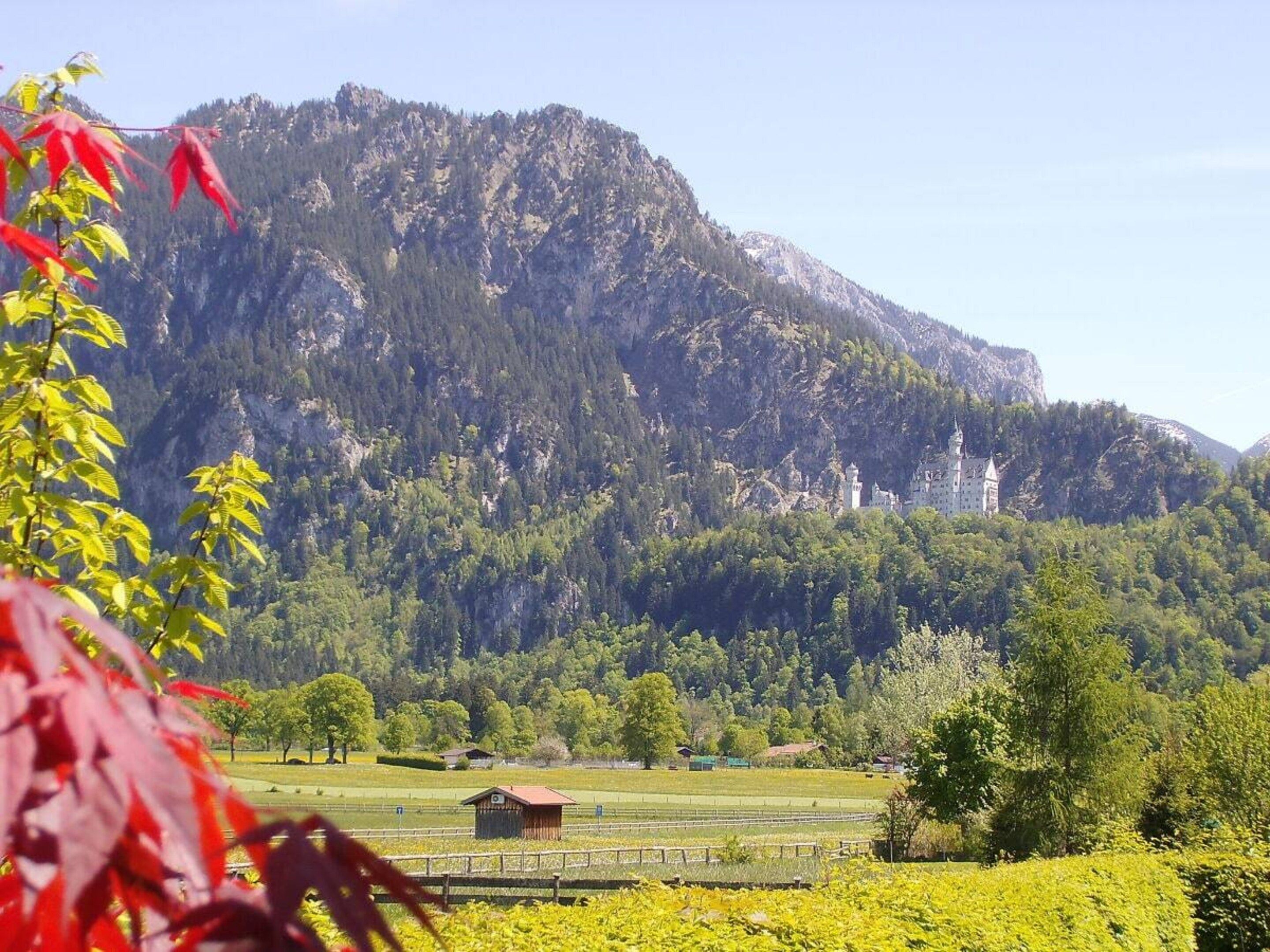 Eine gebirgige Landschaft mit einer schlossartigen Struktur, umgeben von Grünflächen und Feldern.