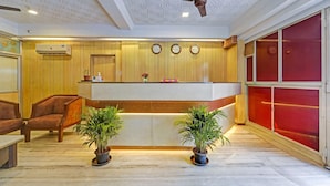 A reception area with a wooden panel wall, a reception desk, two potted plants, a ceiling fan, and a clock on the wall. - GSILVER HOTEL HIMALAYA (Chennai)