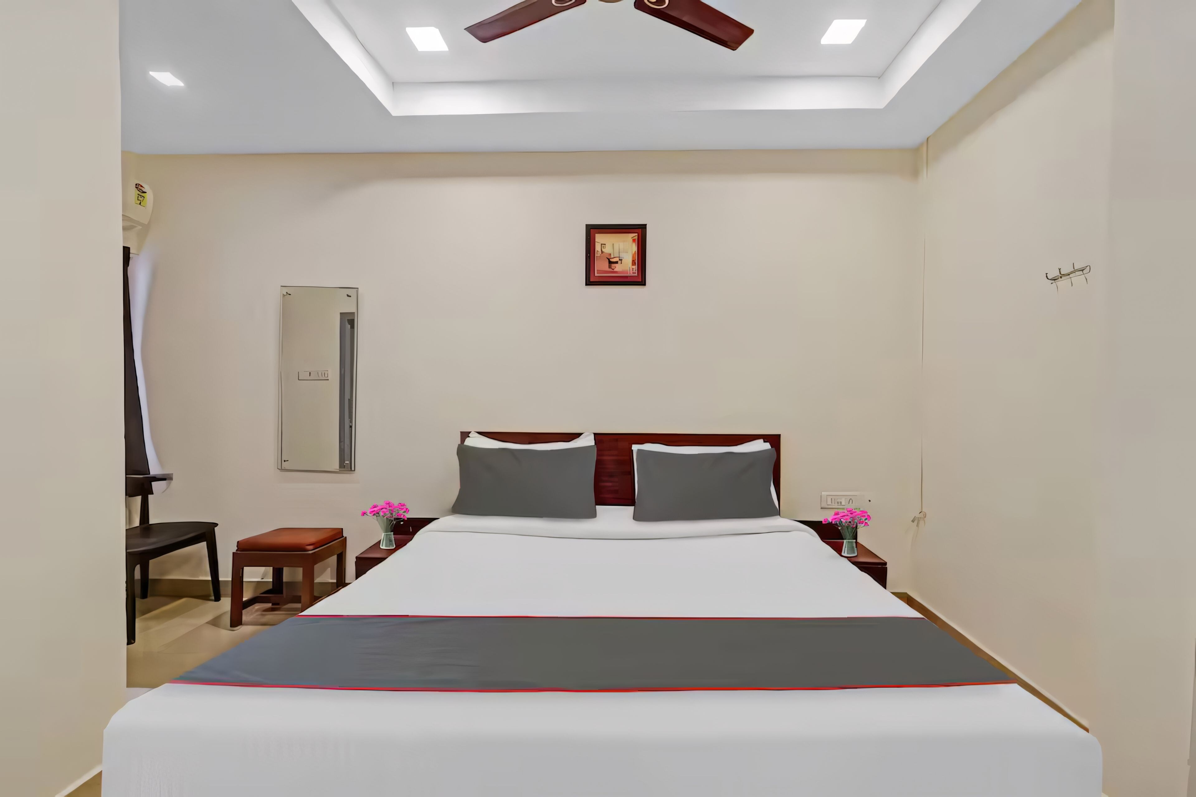 Habitación de hotel con cama, mesitas de noche, un espejo, ventilador de techo y un pequeño cuadro en la pared.