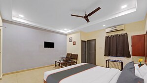 A hotel room with a bed, a desk, a chair, a ceiling fan, an air conditioning unit, and a television. - GSILVER HOTEL HIMALAYA (Chennai)
