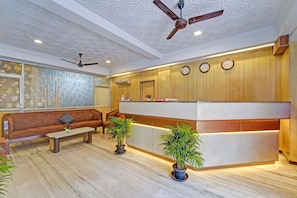 A modern hotel lobby with a reception desk, seating area, ceiling fans, and decorative wall patterns. - GSILVER HOTEL HIMALAYA (Chennai)