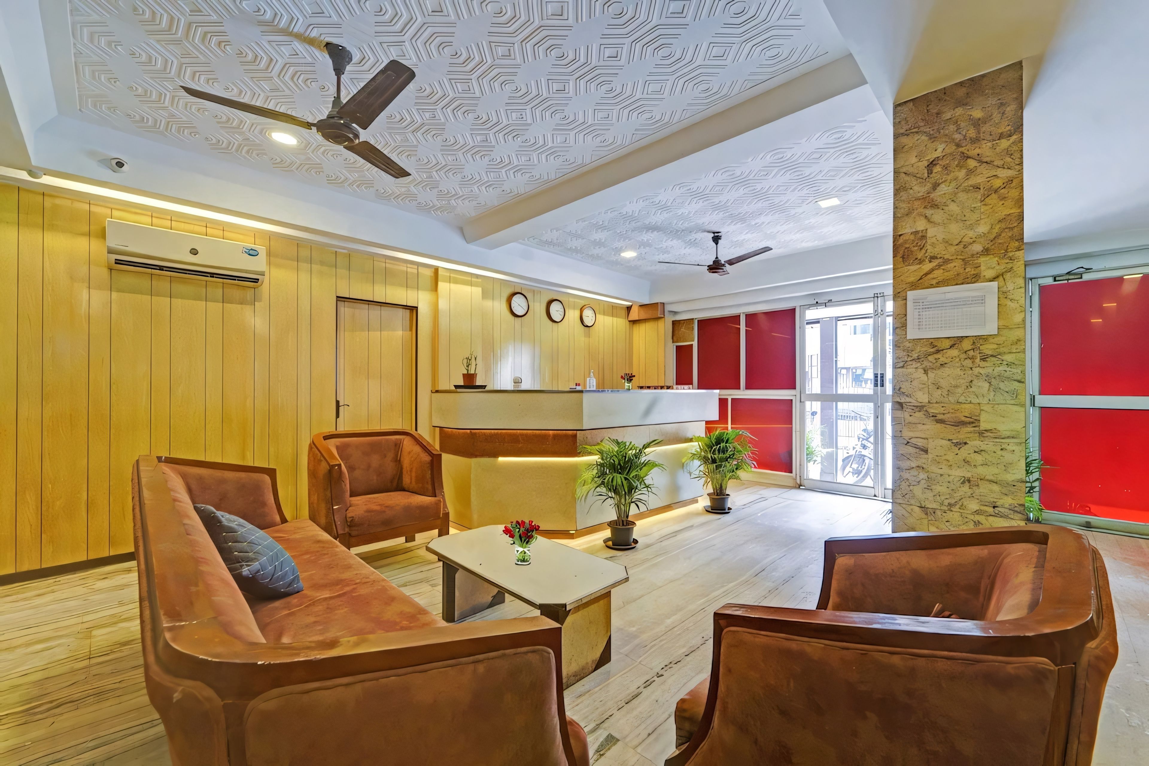 Un vestíbulo de hotel con mostrador de recepción, zona de estar con sofás, ventiladores de techo y un techo con diseño.