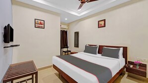 A hotel room with a bed, a desk, a chair, a ceiling fan, and artwork on the walls. - GSILVER HOTEL HIMALAYA (Chennai)