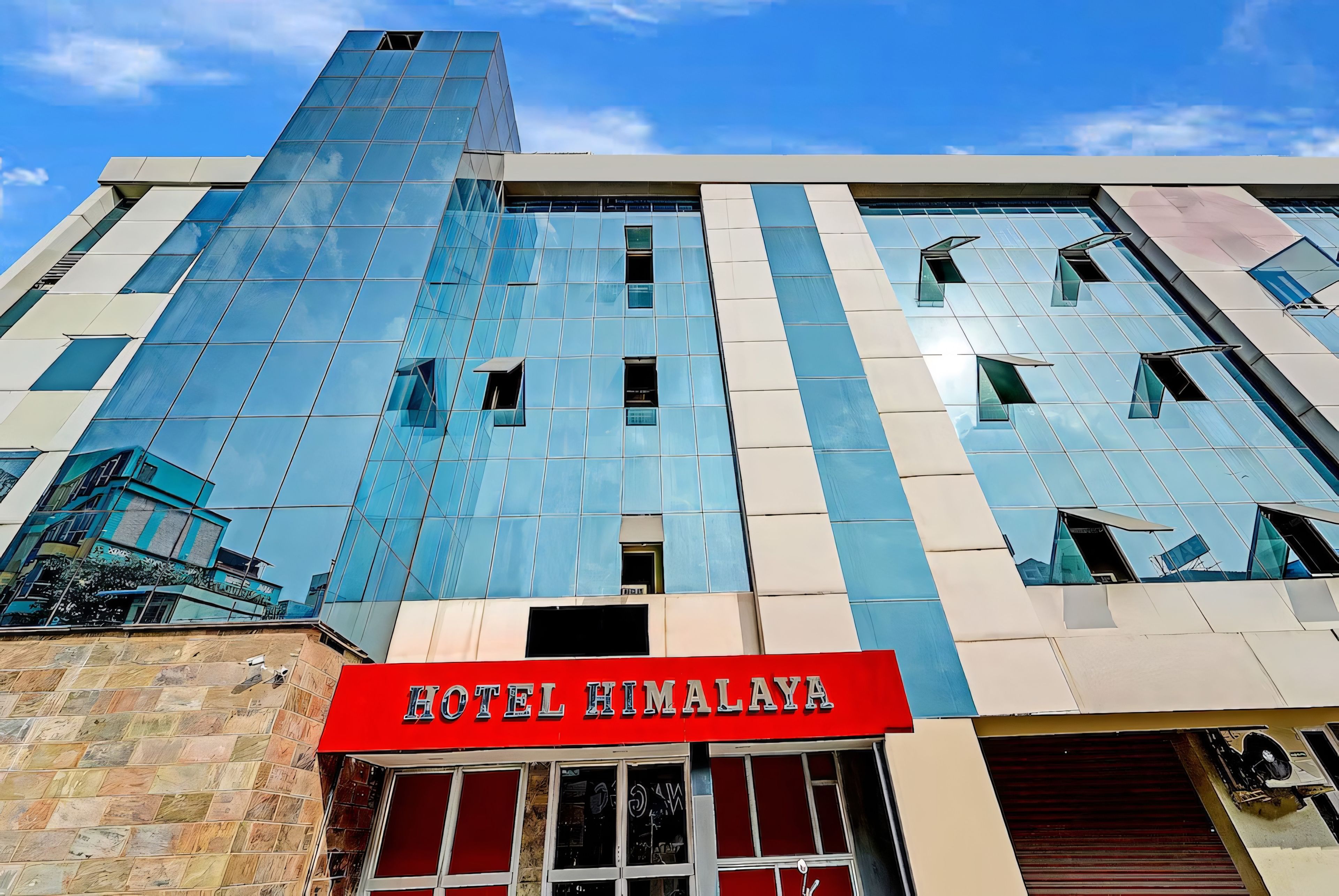 En moderne hotelbygning med en iøjnefaldende glasfacade og et rødt skilt med teksten 'HOTEL HIMALAYA' ved indgangen.
