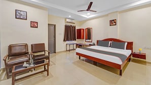 Ein Hotelzimmer mit einem Bett, zwei Stühlen, einem Schreibtisch und einem Deckenventilator.