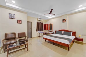 Una habitación de hotel con una cama, dos sillas, un escritorio y un ventilador de techo.